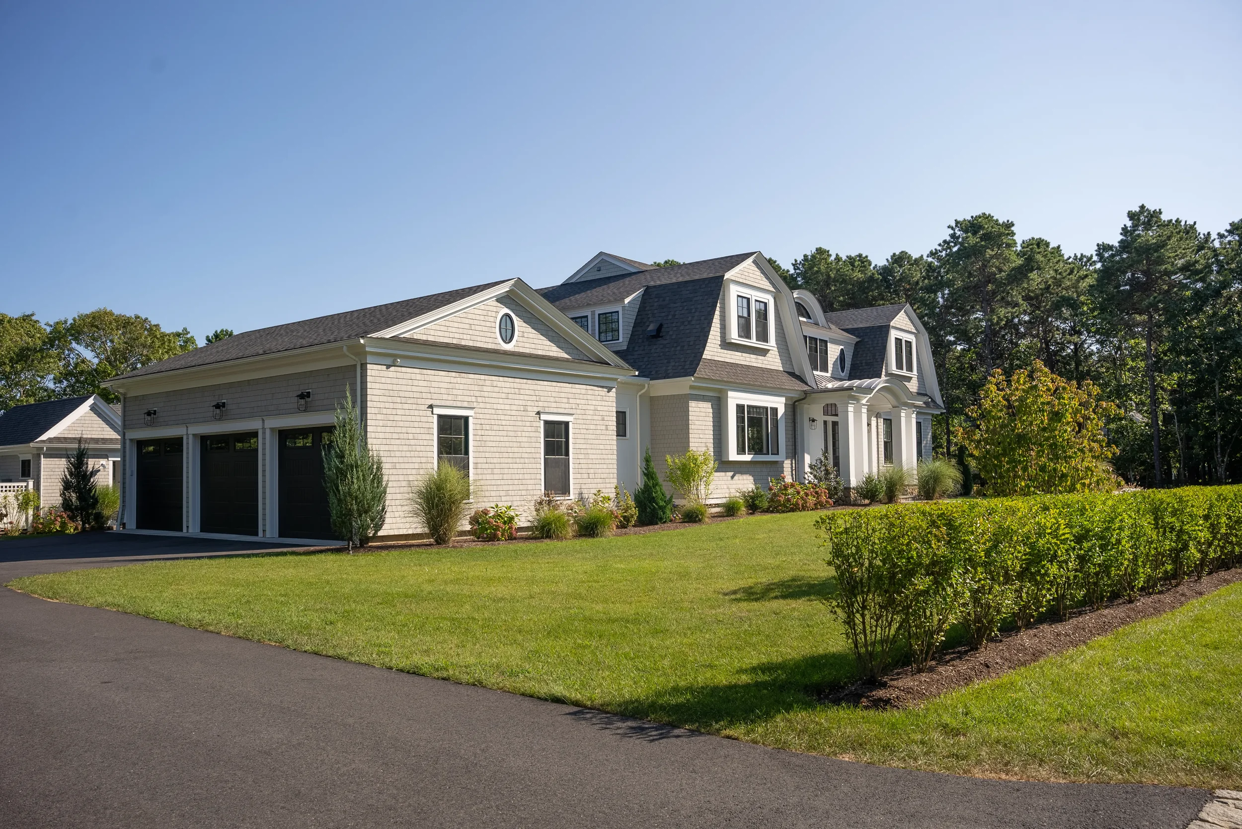 Front view of a large, two-story house with white exterior, black roof, landscaped yard, and a three-car garage.