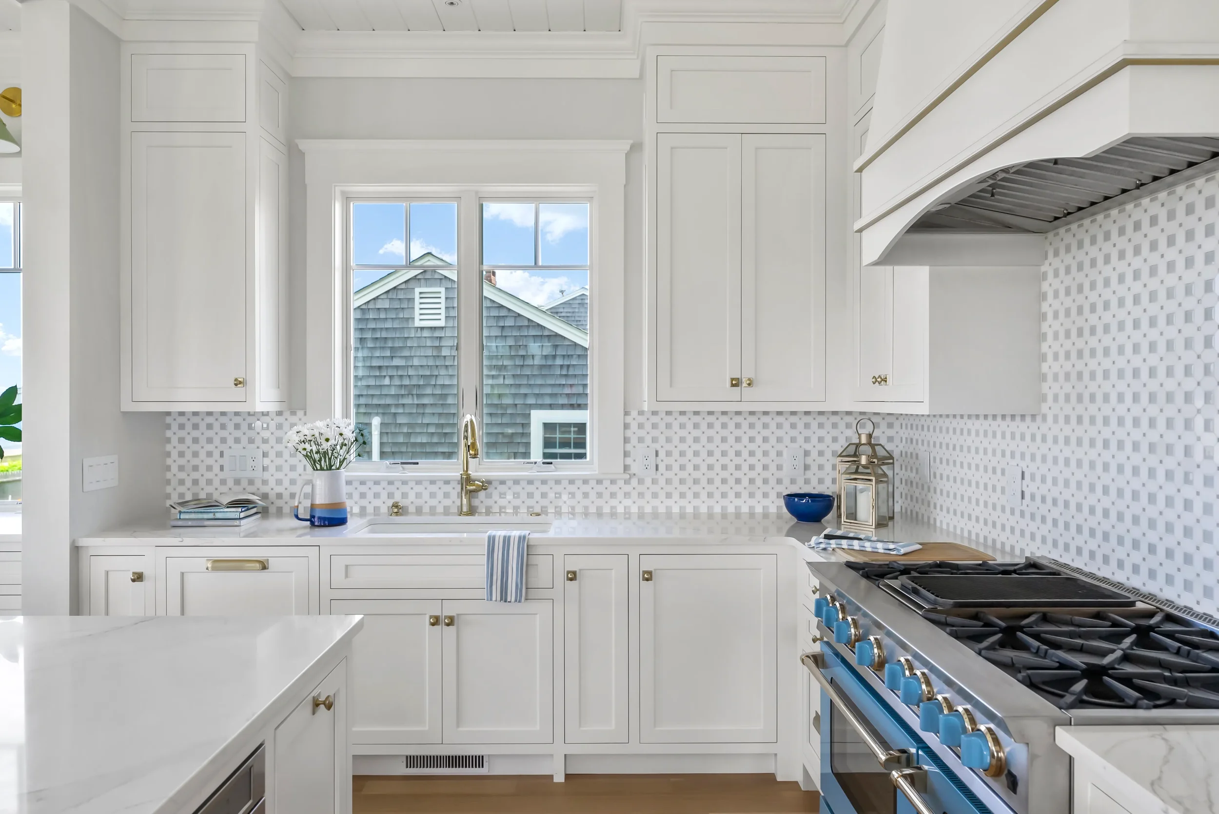 Modern white kitchen with a window above the sink, gold hardware, a blue and white striped towel, and a blue and silver stove.