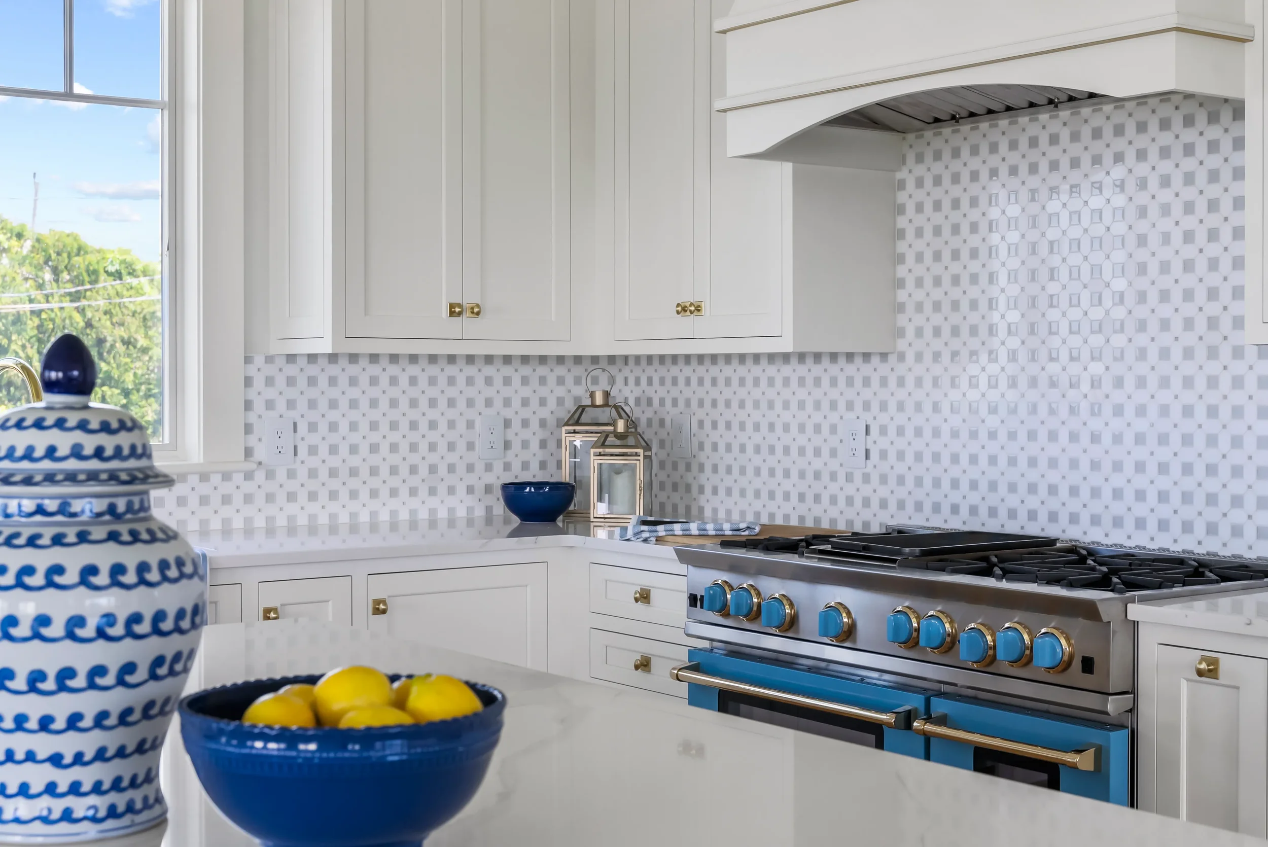Modern white kitchen with gold cabinet handles, blue and yellow accents, and a backsplash with a geometric tile pattern.