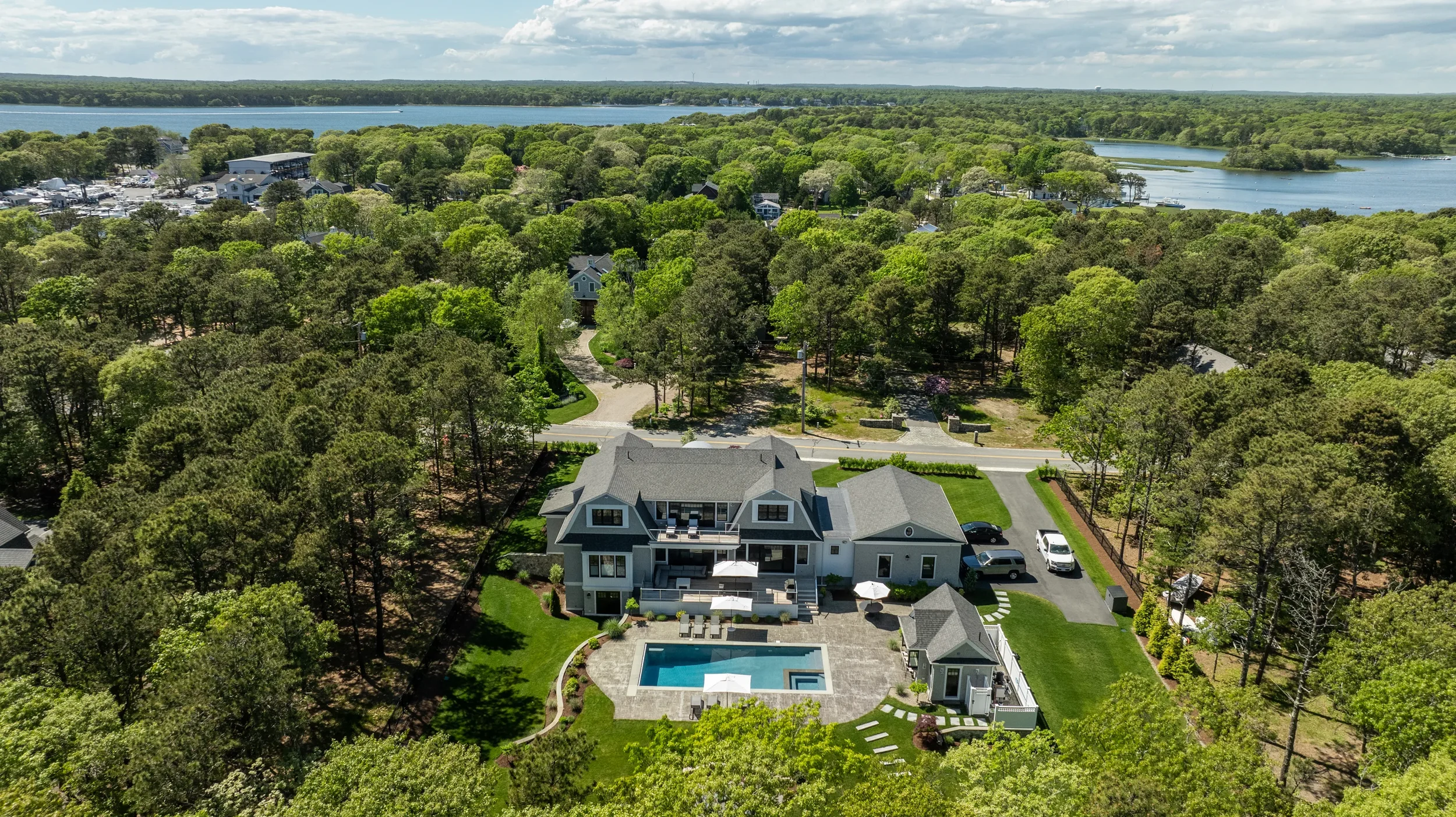 Aerial view of a large residential house with a swimming pool in the backyard, surrounded by trees and greenery, with a lake in the distance.