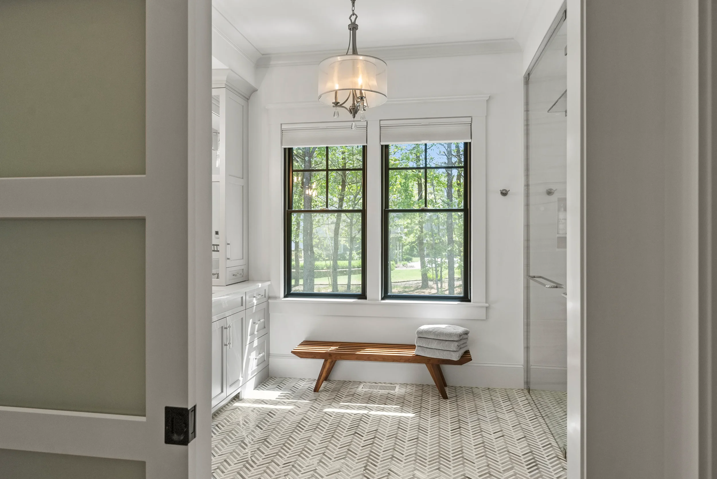 Bright laundry room with large window, white cabinetry, wooden bench, and folded towels.