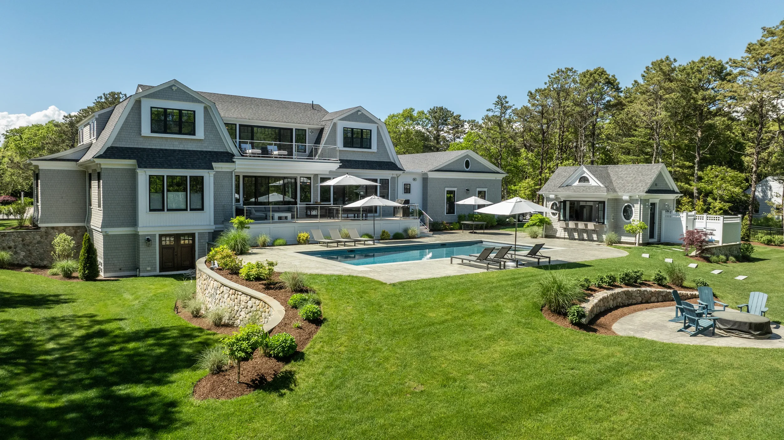 Large backyard with a swimming pool, two gazebos, and a modern house with multiple decks and large windows, surrounded by a well-kept lawn and trees.