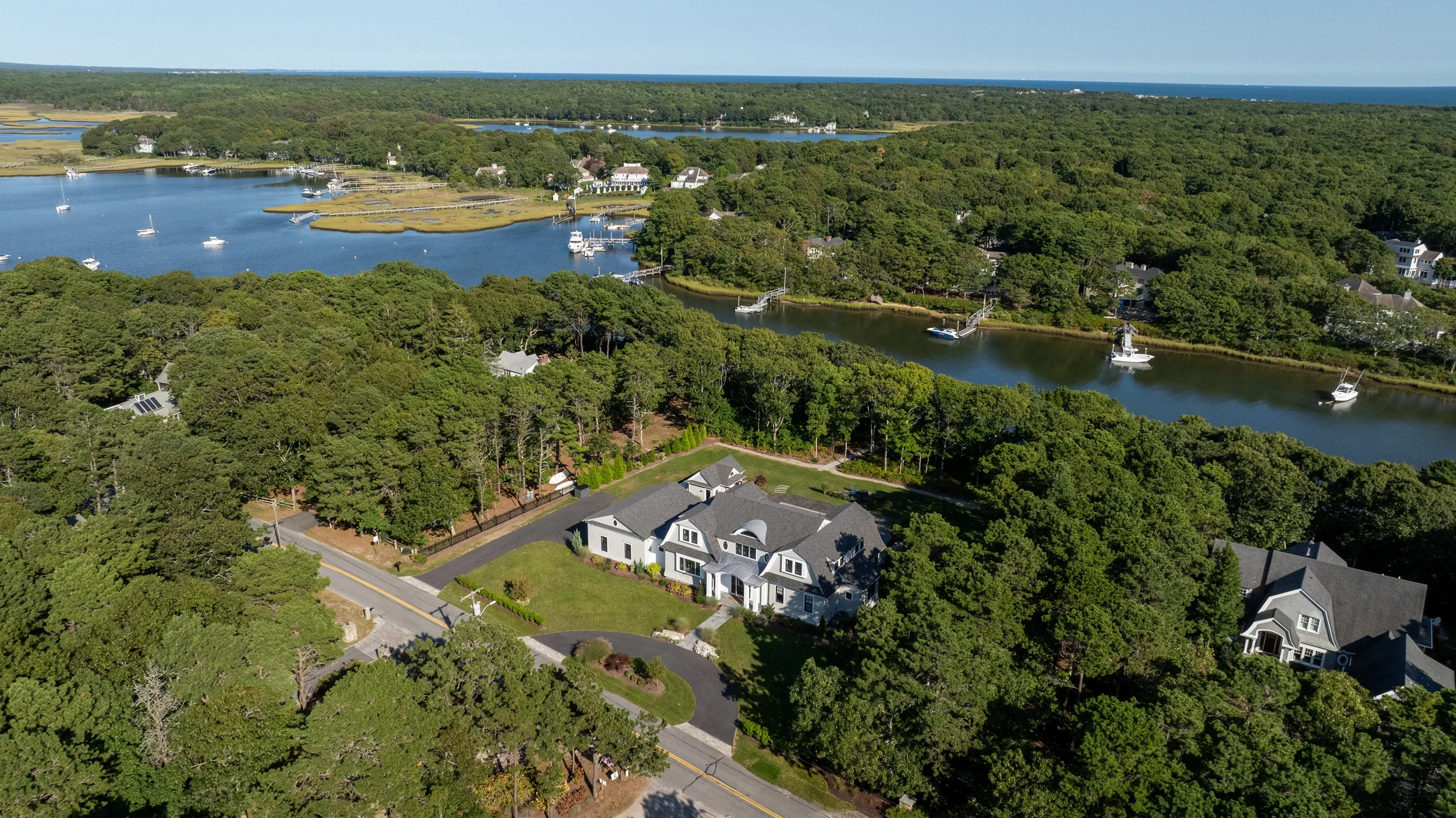 Aerial view of a residential neighborhood with houses, surrounded by dense trees, near a body of water with boats docked along the shoreline.