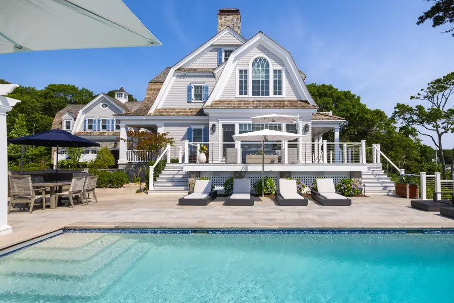 Luxury house with a backyard pool, lounge chairs, and outdoor dining area under umbrellas.