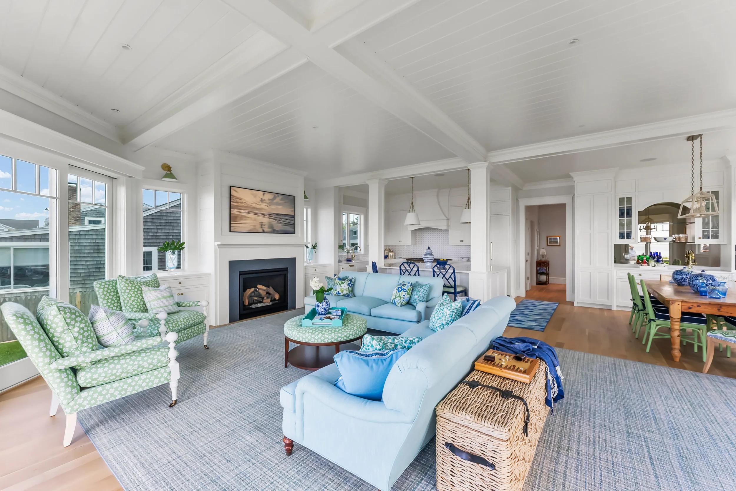 Bright living room with large windows, white walls, and a white ceiling. There are two light green armchairs with white polka dots, a blue sofa, and assorted decorative pillows. A fireplace is centered on the wall with a picture above it. The room op