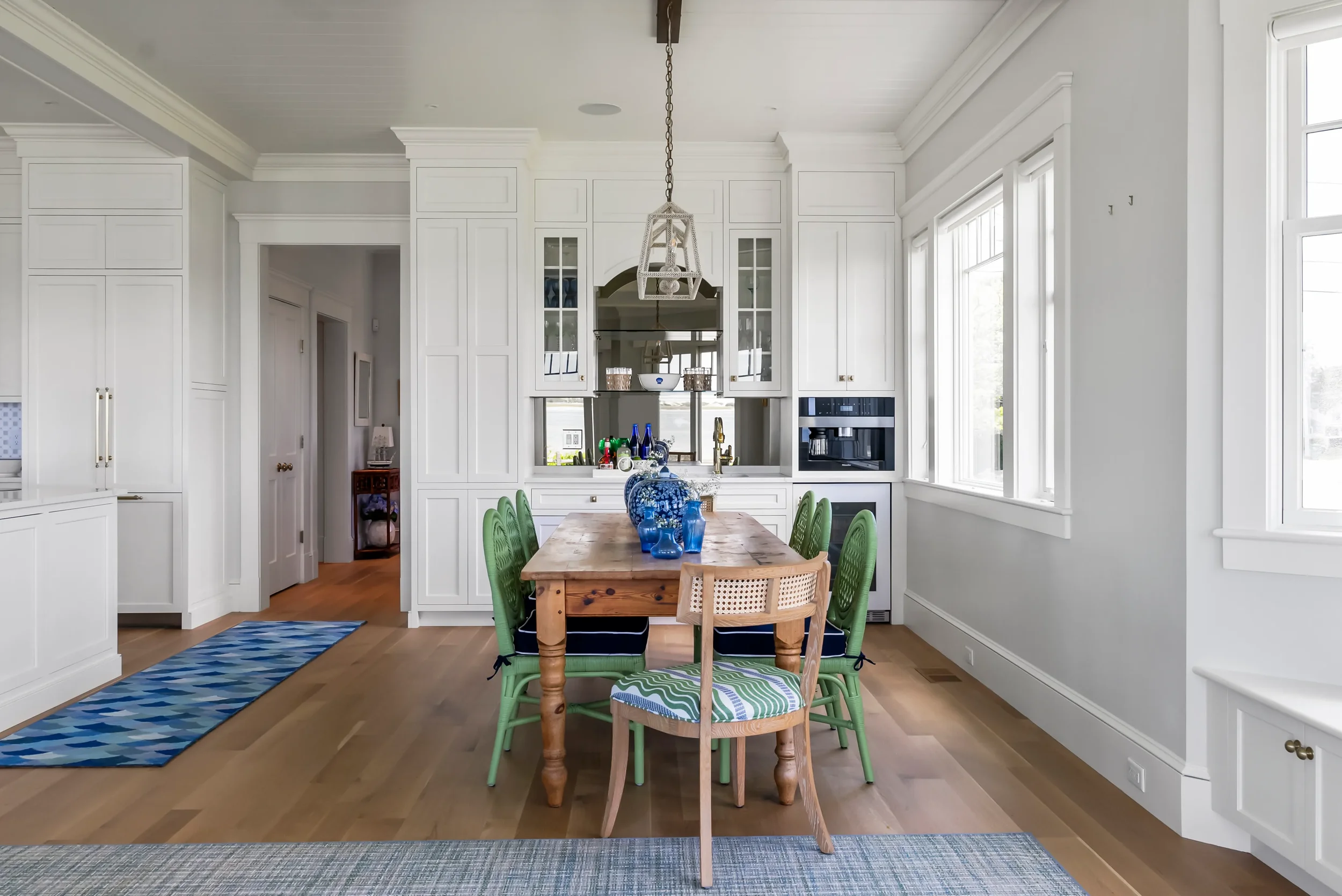 Bright kitchen with white cabinets, large windows, and a wooden dining table with green chairs.