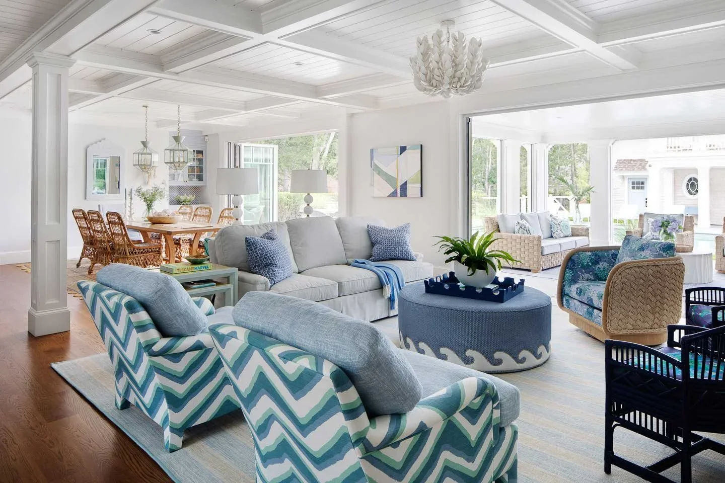 This image captures a stunning coastal-style open-concept living and dining area, designed to evoke lightness, comfort, and a strong connection to the outdoors. The living space features a white sofa adorned with blue accent pillows, a round ottoman