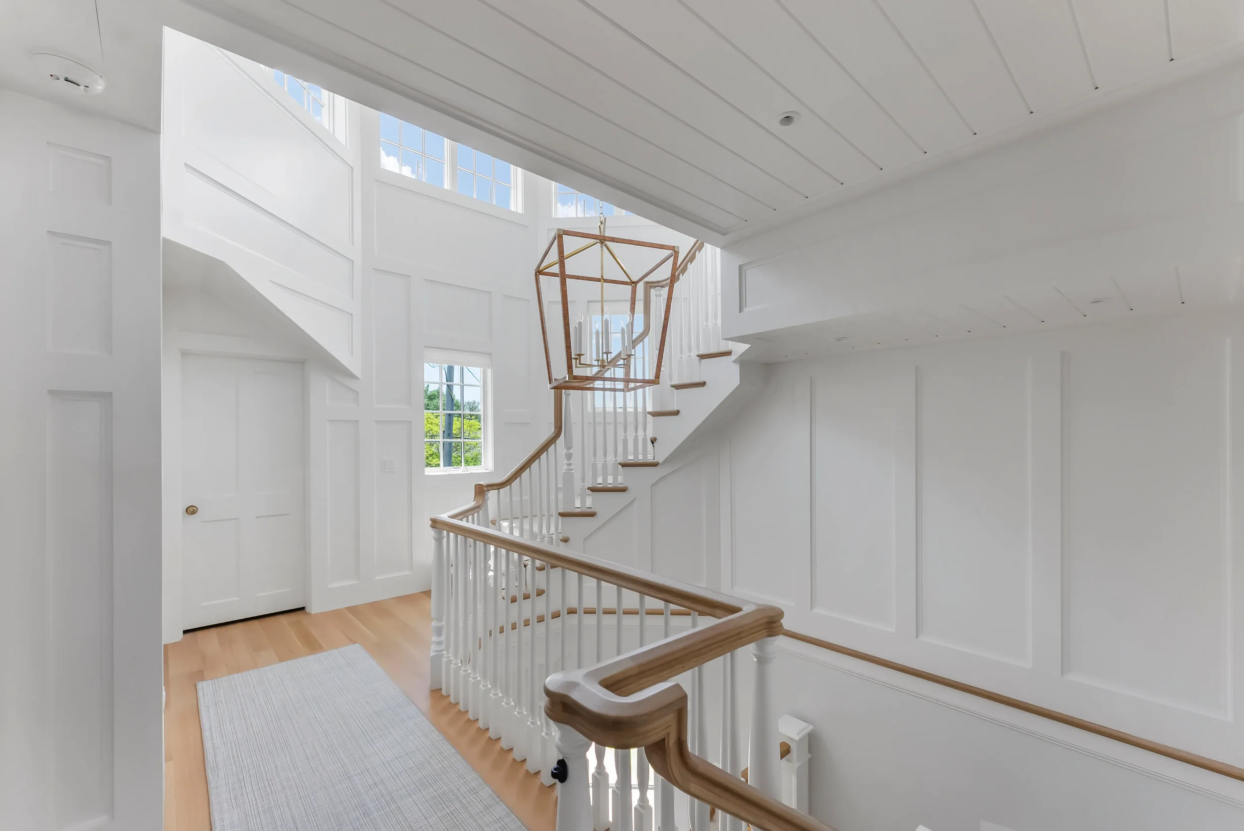 Bright entryway with white walls, wooden staircase, large windows, and modern chandelier.