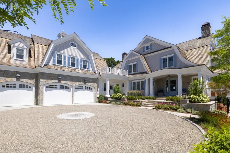 A large, upscale house with a stone and siding exterior, multiple garage doors, and a landscaped front yard with flower beds and steps leading to the front porch.
