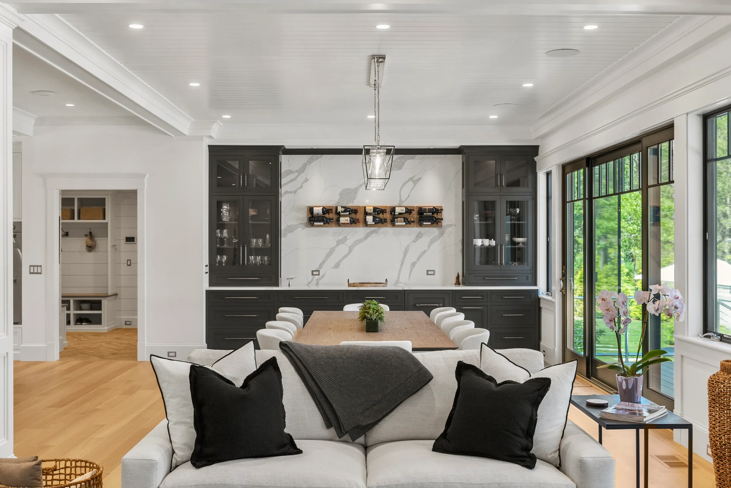 Modern dining and living room with black cabinetry and large windows showing greenery outside.