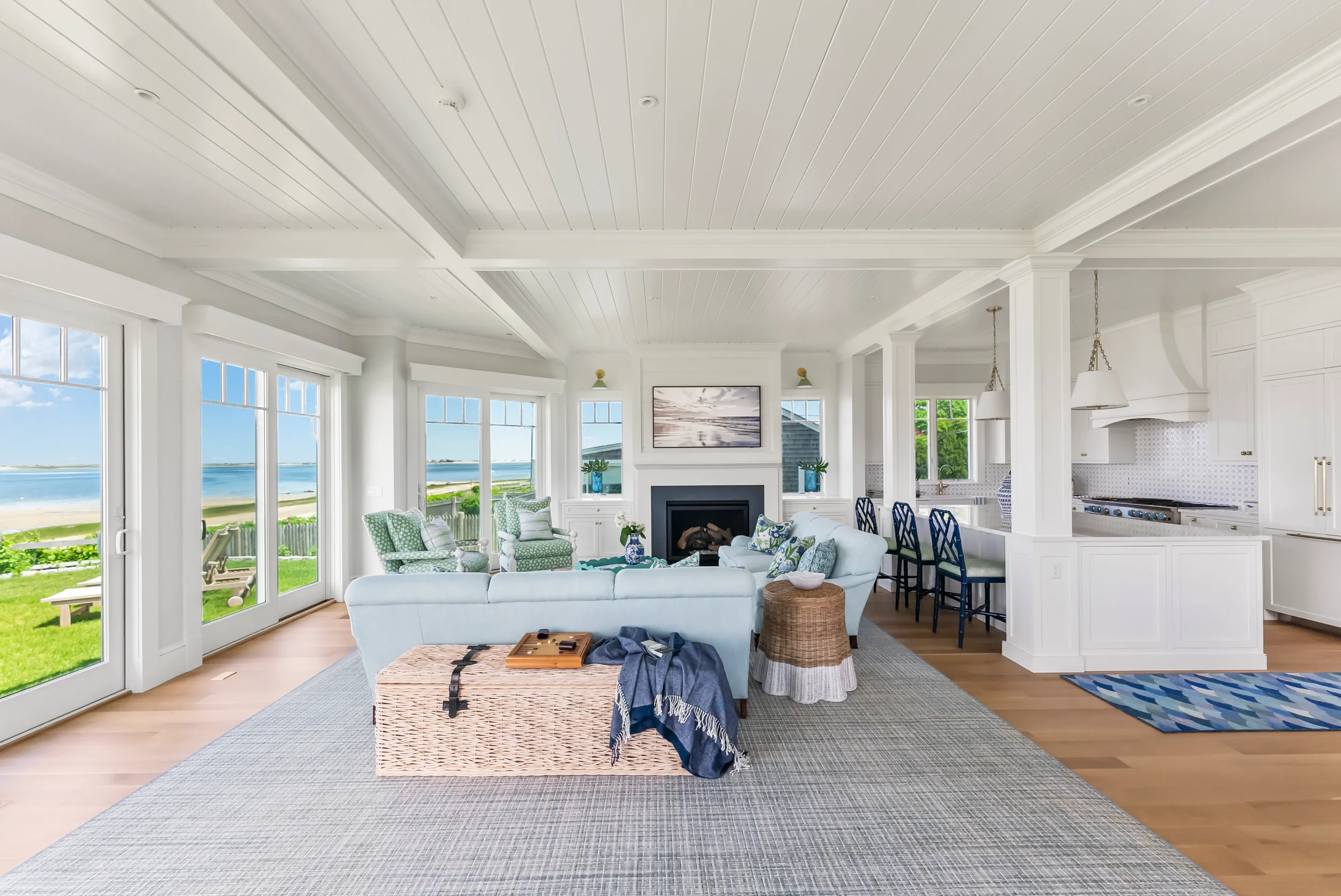 Bright living room with large windows overlooking a beach, white walls and ceiling, light-colored furniture, a fireplace, and a view of the ocean through the glass doors.