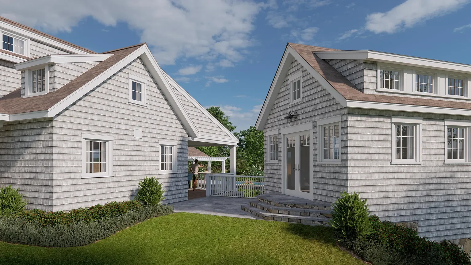 Two houses with grey shingle siding and brown shingle roofs, separated by a small yard with grass and bushes, under a partly cloudy sky.