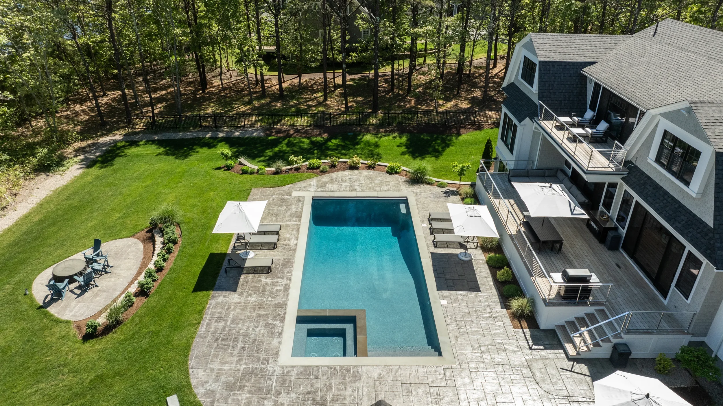 Aerial view of a modern backyard with a swimming pool, shaded seating areas, landscaped garden, and surrounding trees.