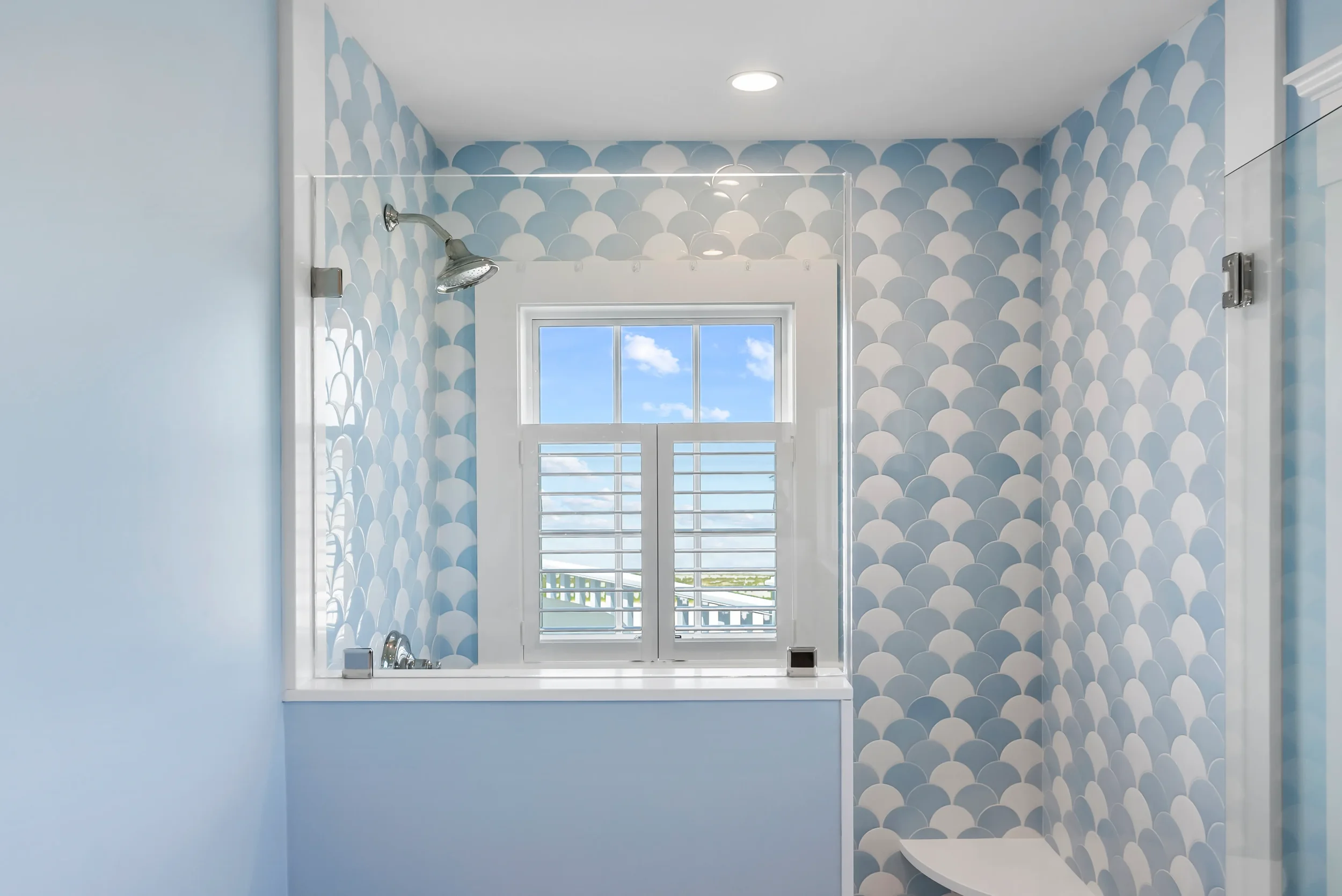 Bathroom with blue scalloped tile walls, a small window showing a blue sky with clouds, and a walk-in shower area.