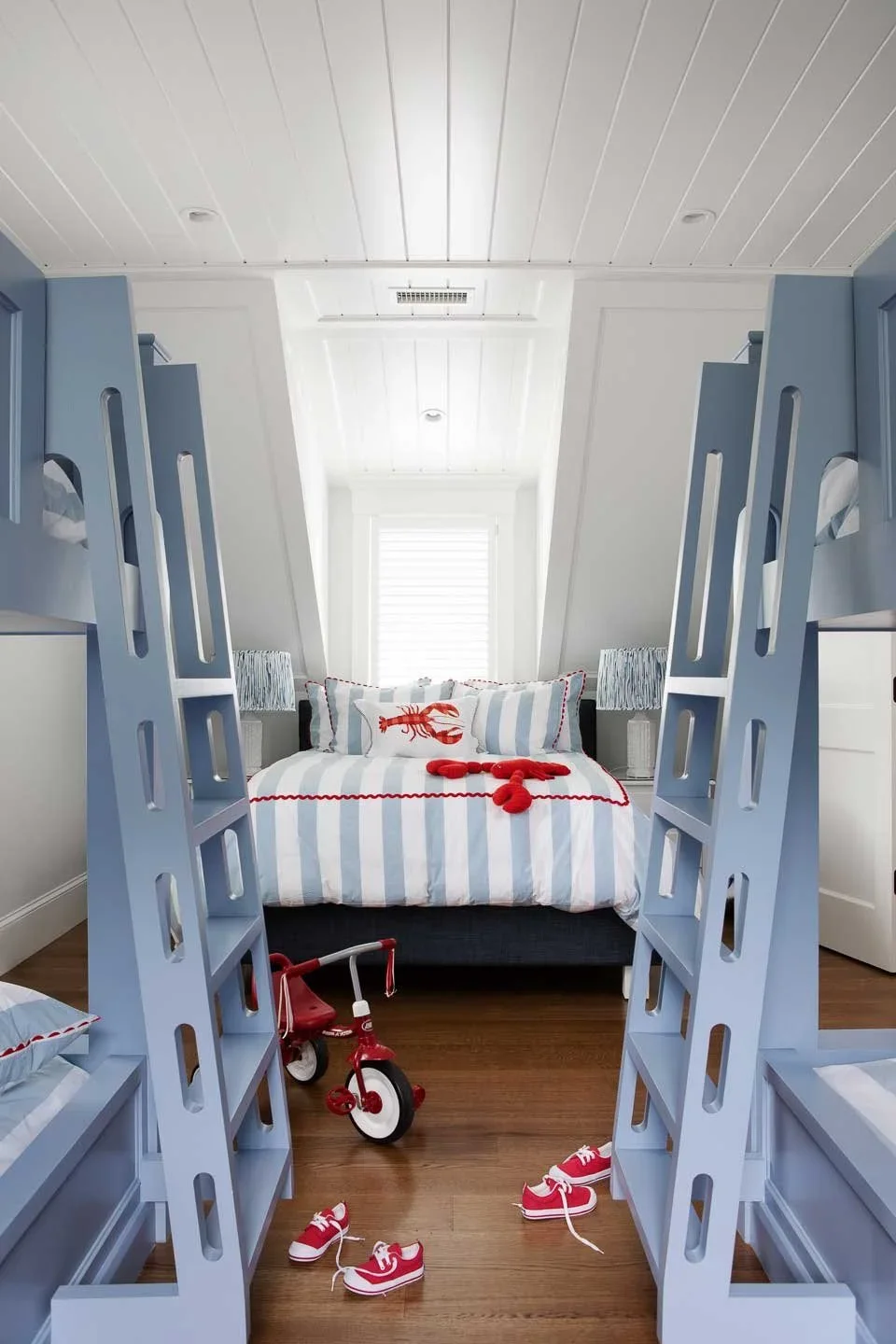 This image presents a charming children's bedroom with a nautical theme, blending playful elements with crisp, structured design. The room features two sets of blue bunk beds positioned symmetrically on either side, each equipped with built-in ladder