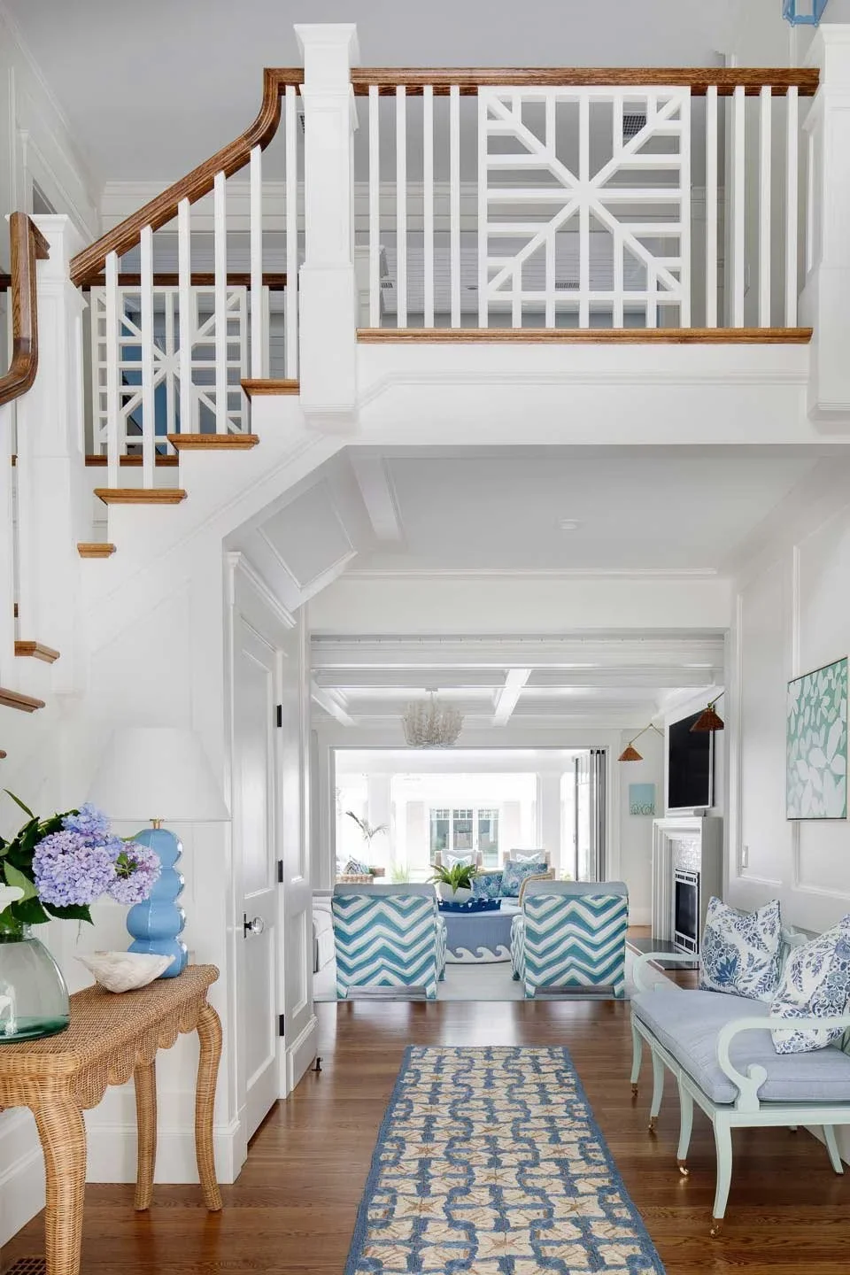 This image portrays a beautifully curated coastal-style interior that exudes freshness and tranquility. The color palette is dominated by soft whites and pastel blues, creating an airy, inviting atmosphere. In the foreground, a wooden console table w