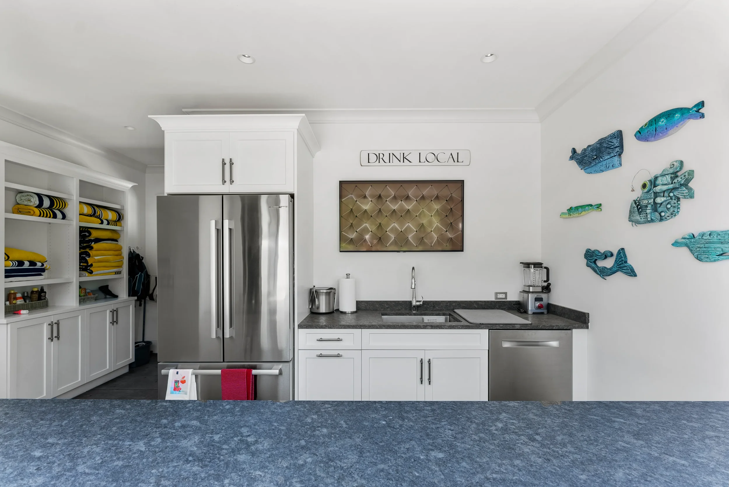 A modern kitchen with white cabinets, stainless steel appliances, black countertops, and decorative fish wall art.