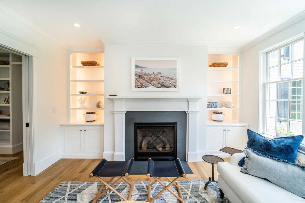 Living room with white walls, built-in shelves, fireplace, overlooking a large window, and a white couch with blue pillows.