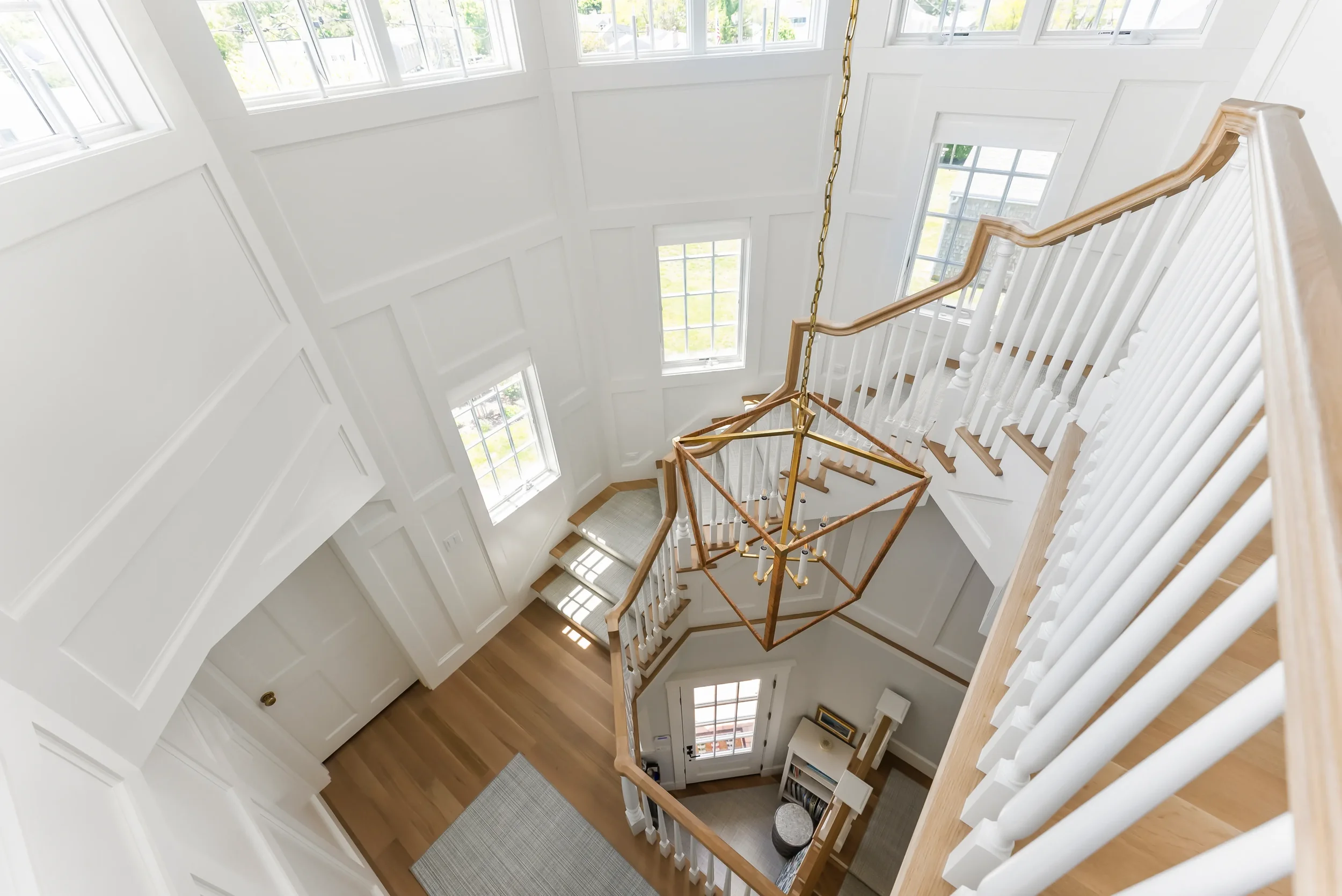 View of a bright second-story foyer with a staircase, large windows, and a modern geometric chandelier.