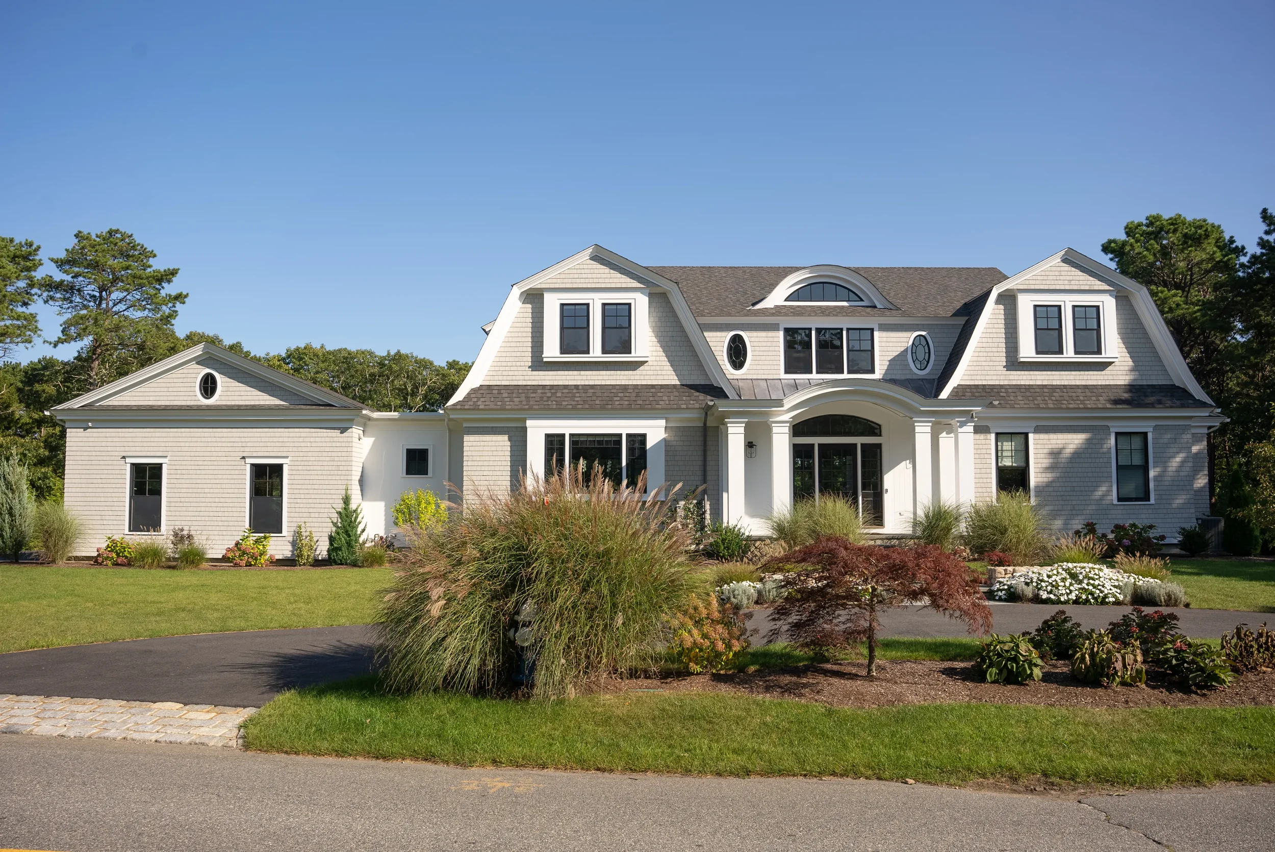 A large white two-story house with decorative windows and a landscaped front yard under a clear blue sky.