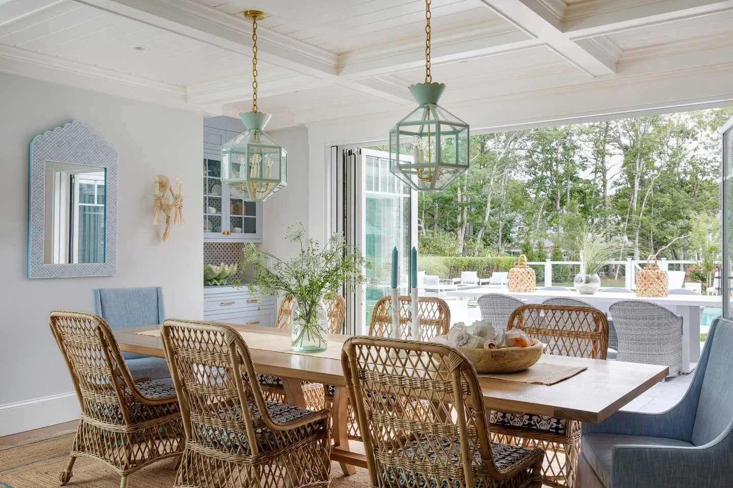This image captures a serene and stylish dining area that seamlessly connects indoor elegance with outdoor leisure. At the heart of the space is a wooden dining table surrounded by intricately woven wicker chairs, offering a natural texture that comp