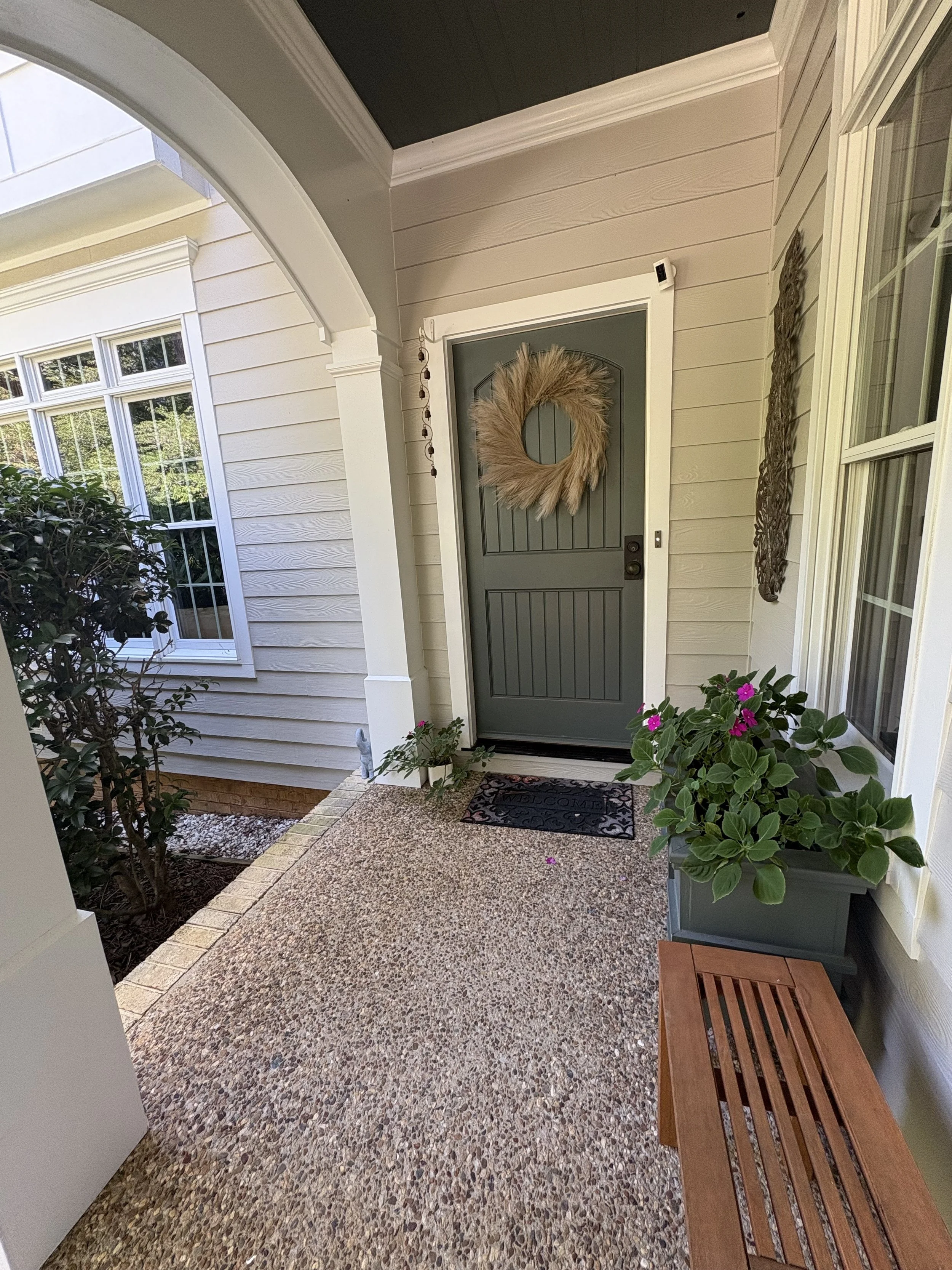 Front porch with a green door, a decorative wreath, potted plants, a welcome mat, and a wooden bench.