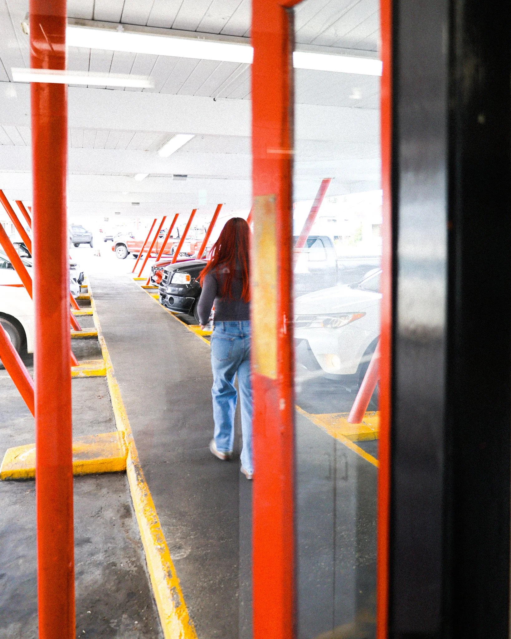 A person with long red hair, wearing a dark top and blue jeans, walking out to serve customers at Boomers Drive In in Bellingham, WA.