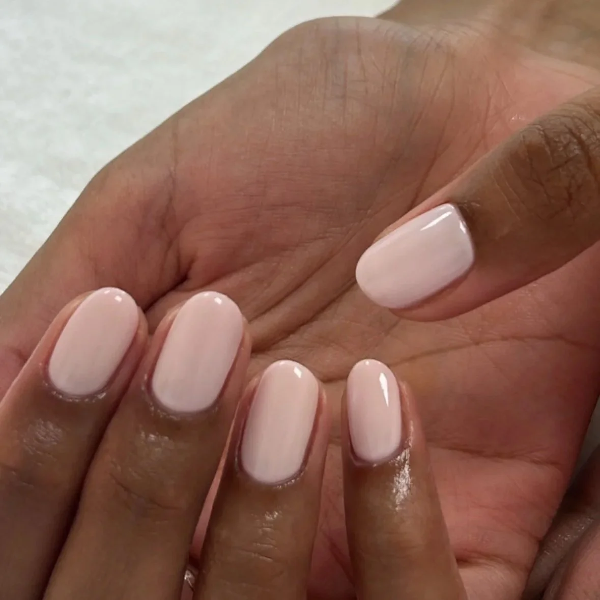 Close-up of a hand with freshly polished light pink fingernails.