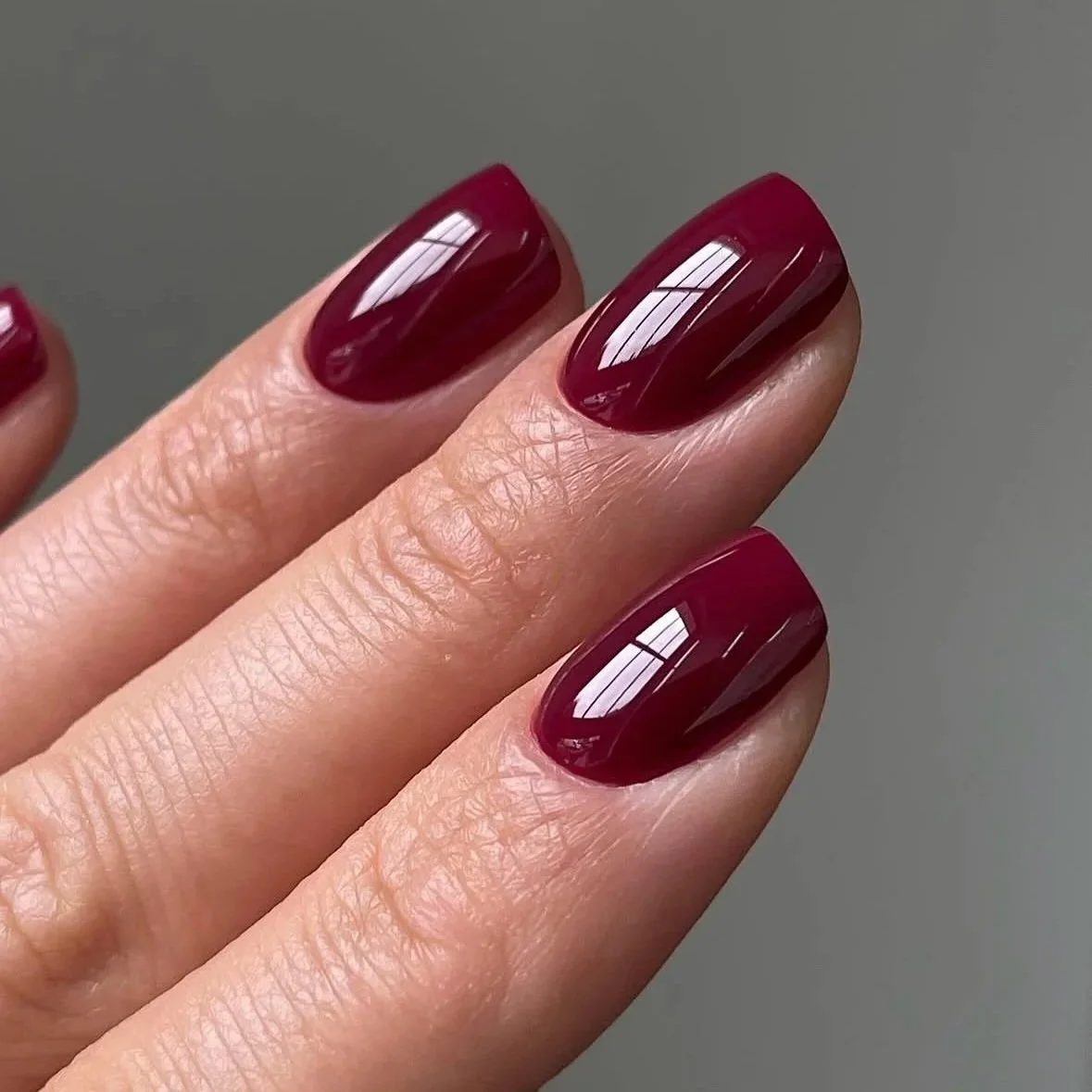 Close-up of fingers with dark red, glossy painted nails against a neutral background.