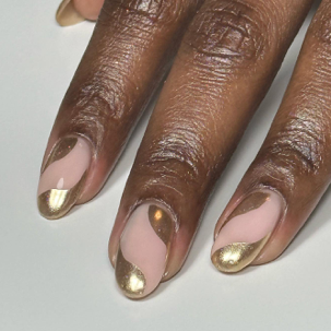 Close-up of a hand with neatly manicured nails painted in a nude color with metallic gold tips.