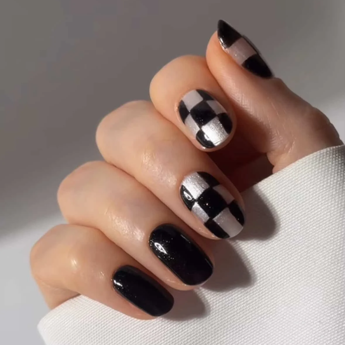 Close-up of a hand with manicured nails painted in black and silver color, featuring a checkered pattern on some nails.