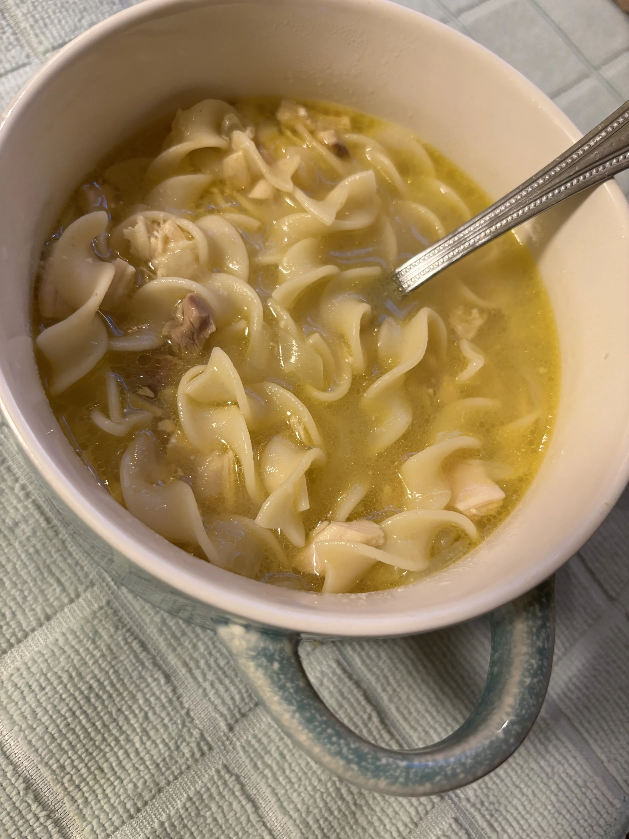 A bowl of chicken noodle soup with tortellini, chicken pieces, and broth on a textured table surface.