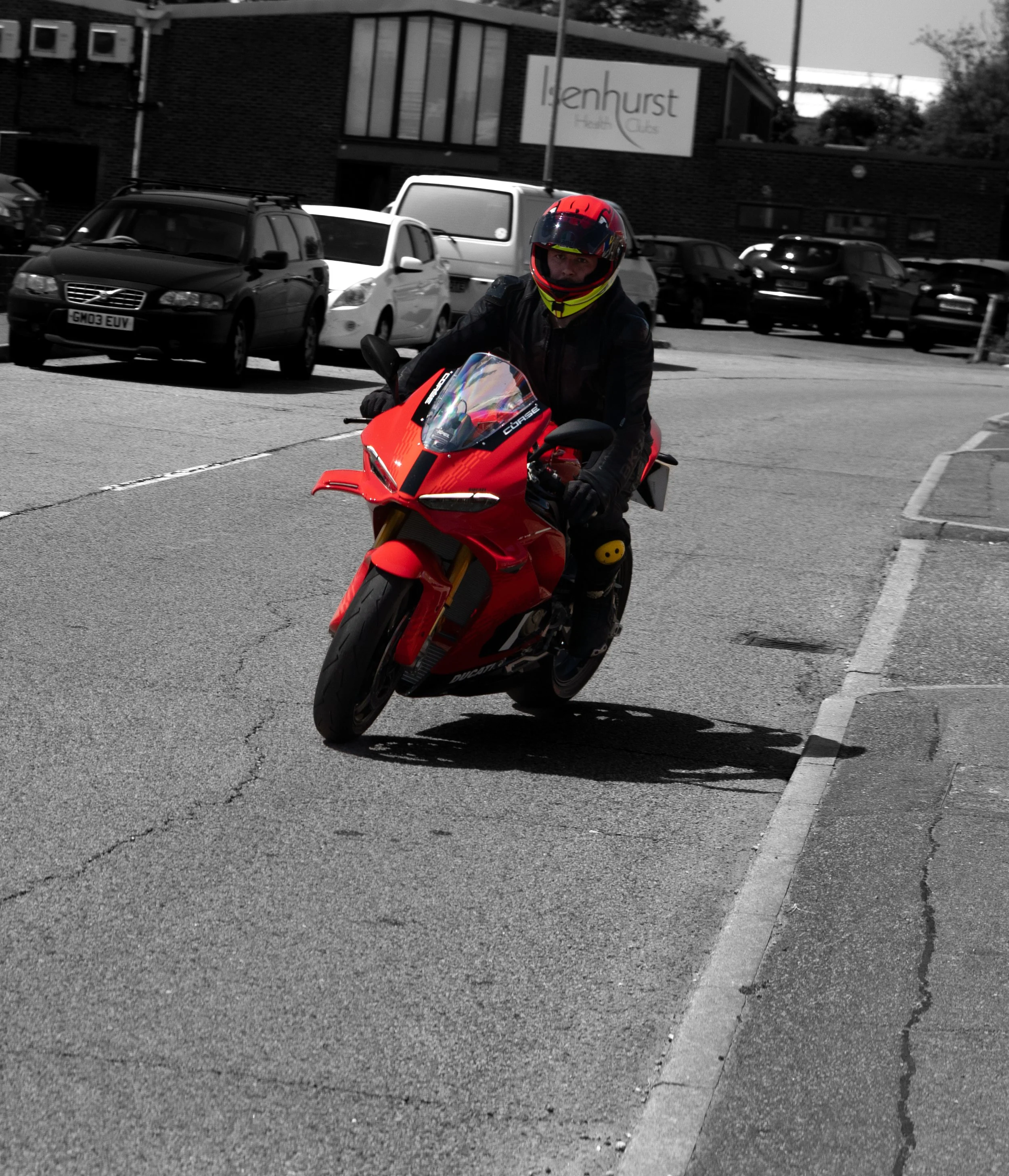 A person wearing a red and black helmet riding a red Ducati motorcycle on a city street, The image has a selective color effect, highlighting the motorcycle and rider.