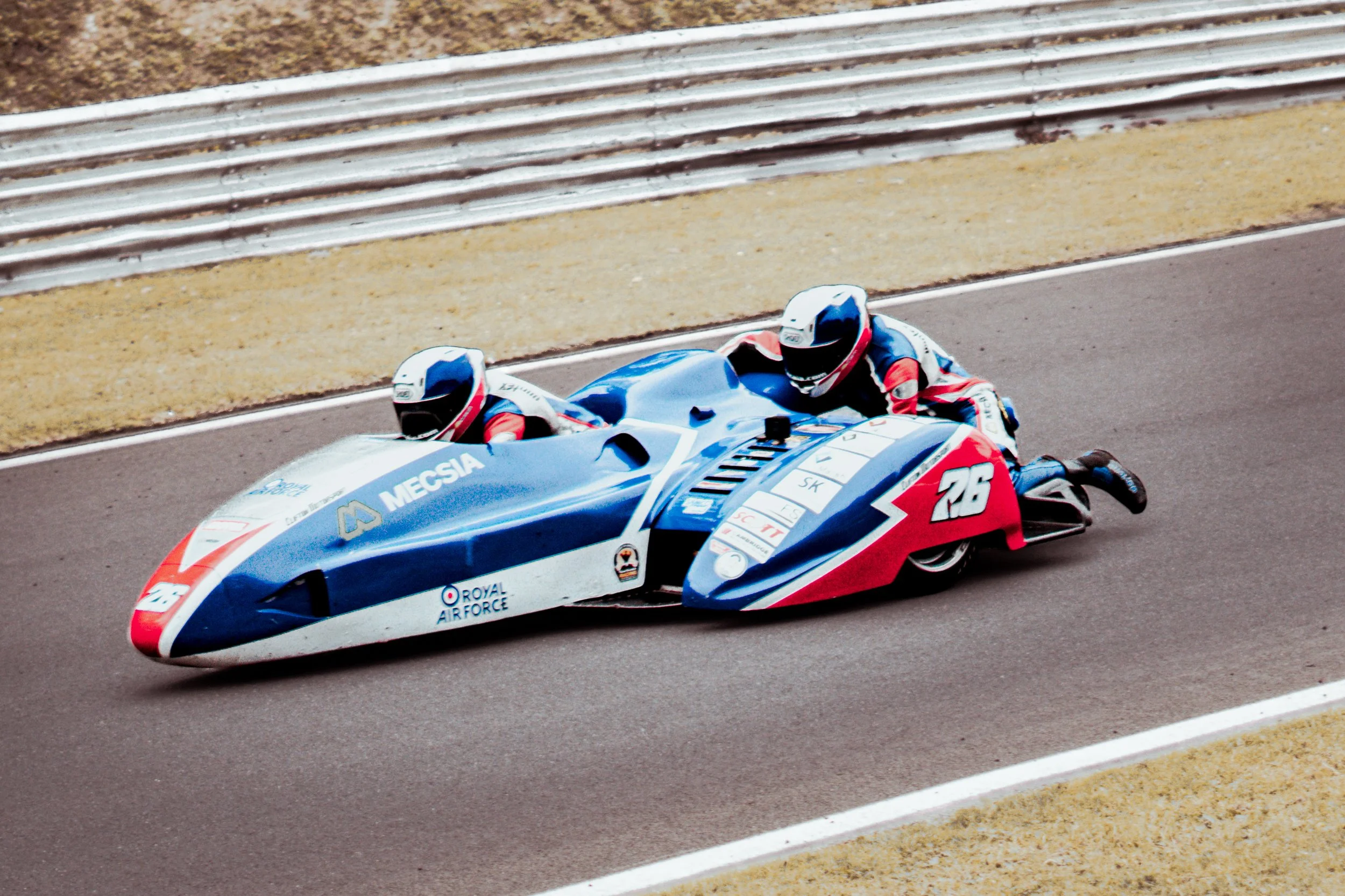 A blue and white racing motorcycle with two riders wearing racing suits and helmets, speeding along a race track.