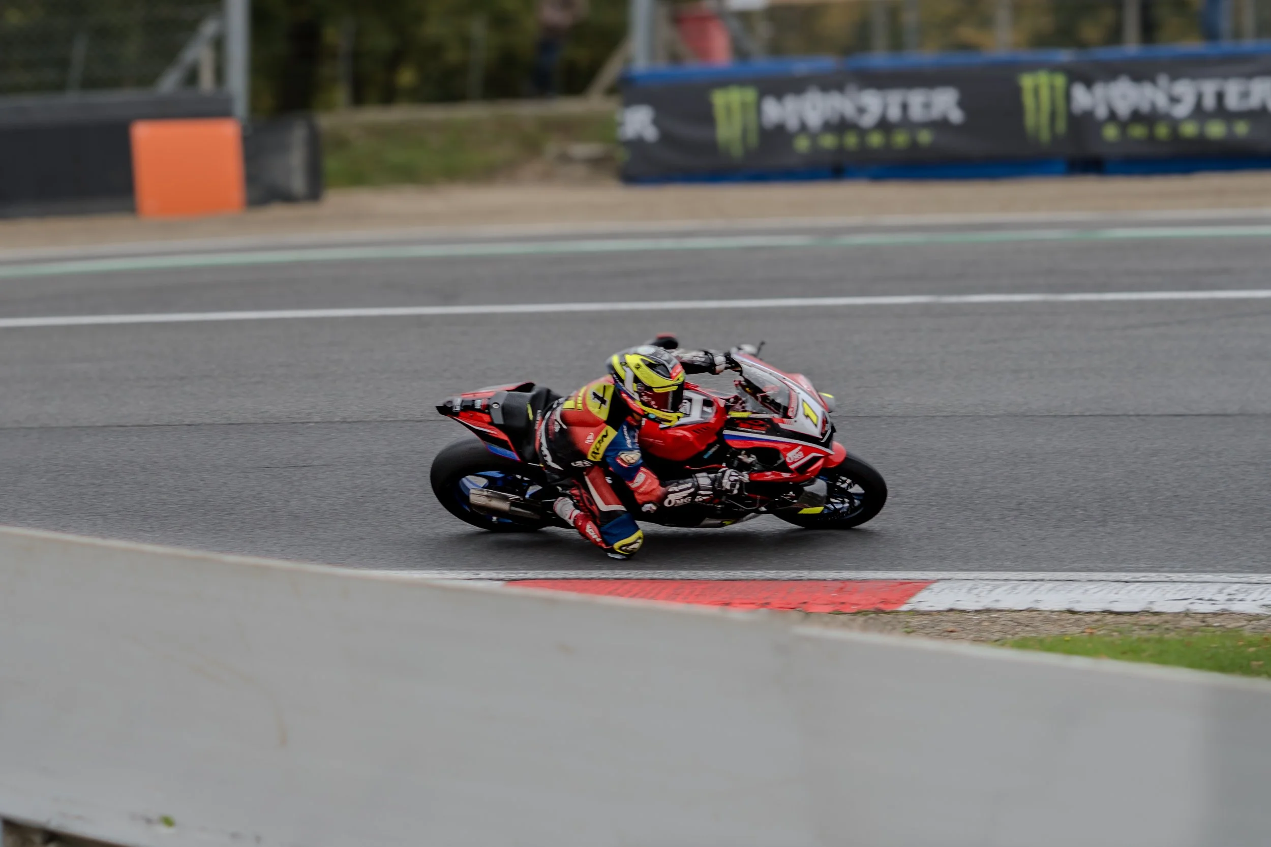 A professional motorcycle racer in a colorful racing suit and helmet leaning into a turn on a race track.
