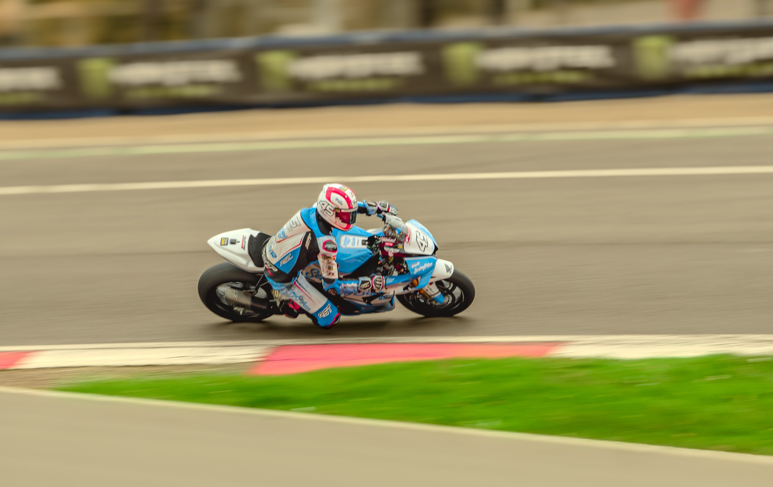 Motorcycle rider in racing gear leaning into a turn on a race track.
