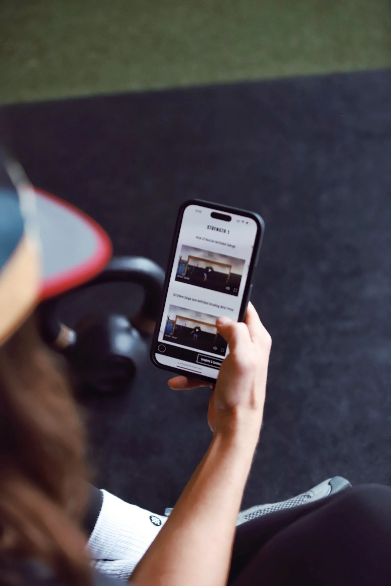 Person holding a smartphone and watching a video tutorial about strength exercises while seated on the floor.