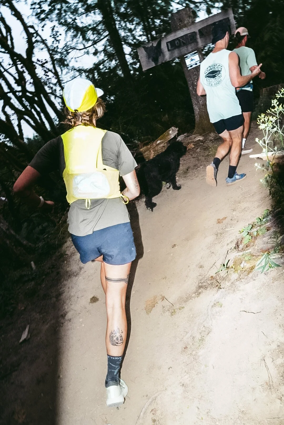 People running on a trail in a wooded area, with one person walking a dog.