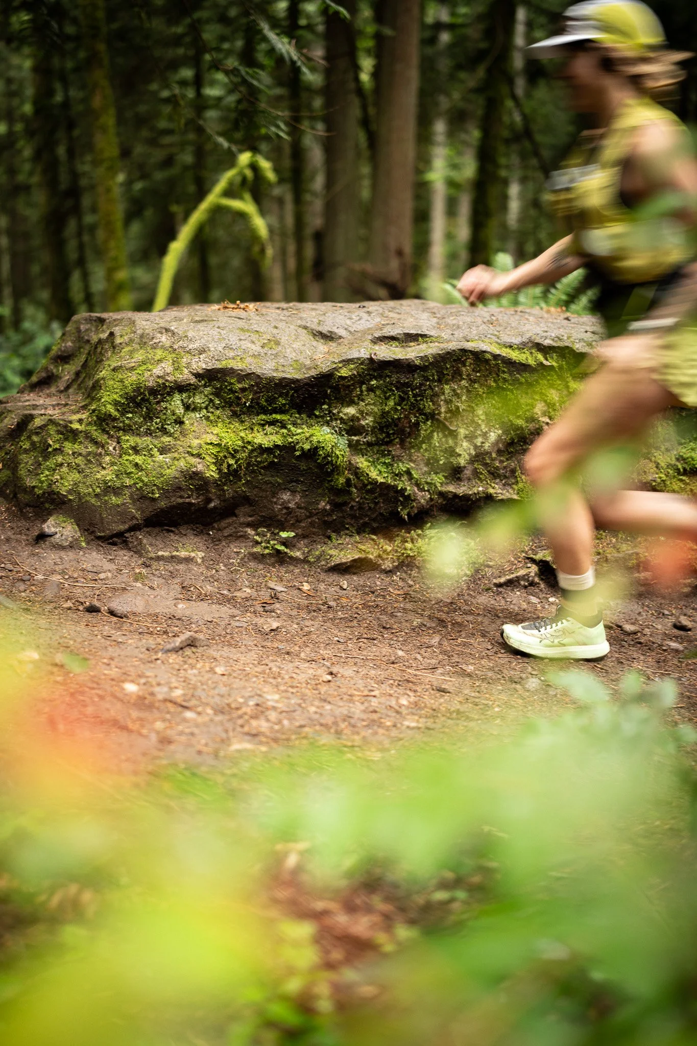 Person running on a forest trail near a moss-covered rock.