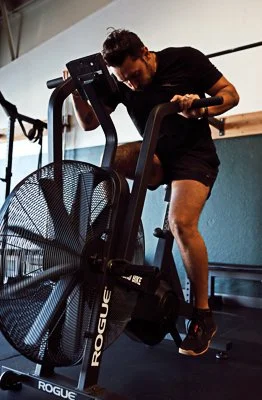 A woman on an exercise bike in a gym, wearing a black shirt and shorts.