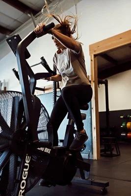 Woman working out on a stationary bike in a gym, her hair flying as she pedals hard.