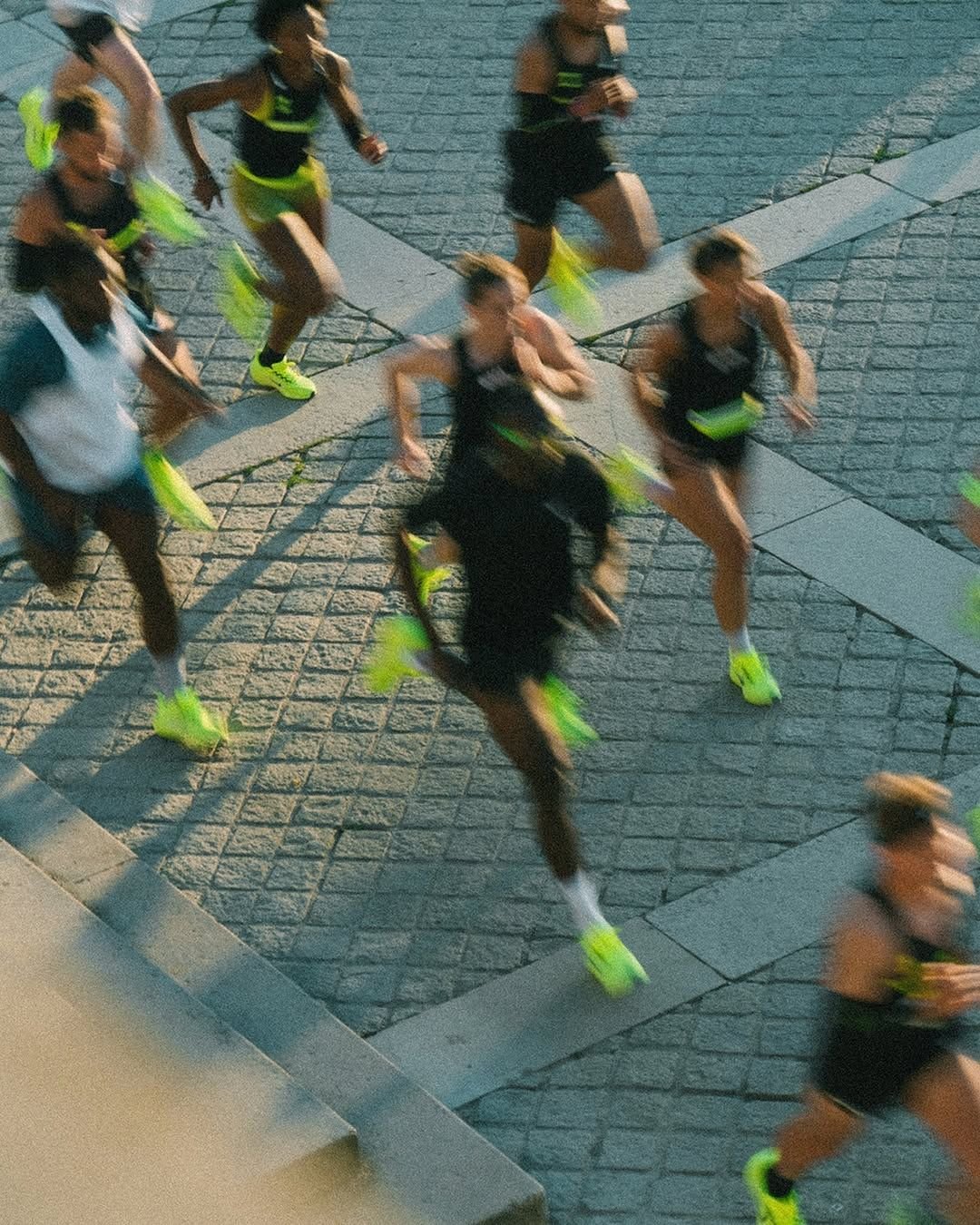 A group of runners in black athletic attire and neon yellow shoes participating in a race on a paved road.