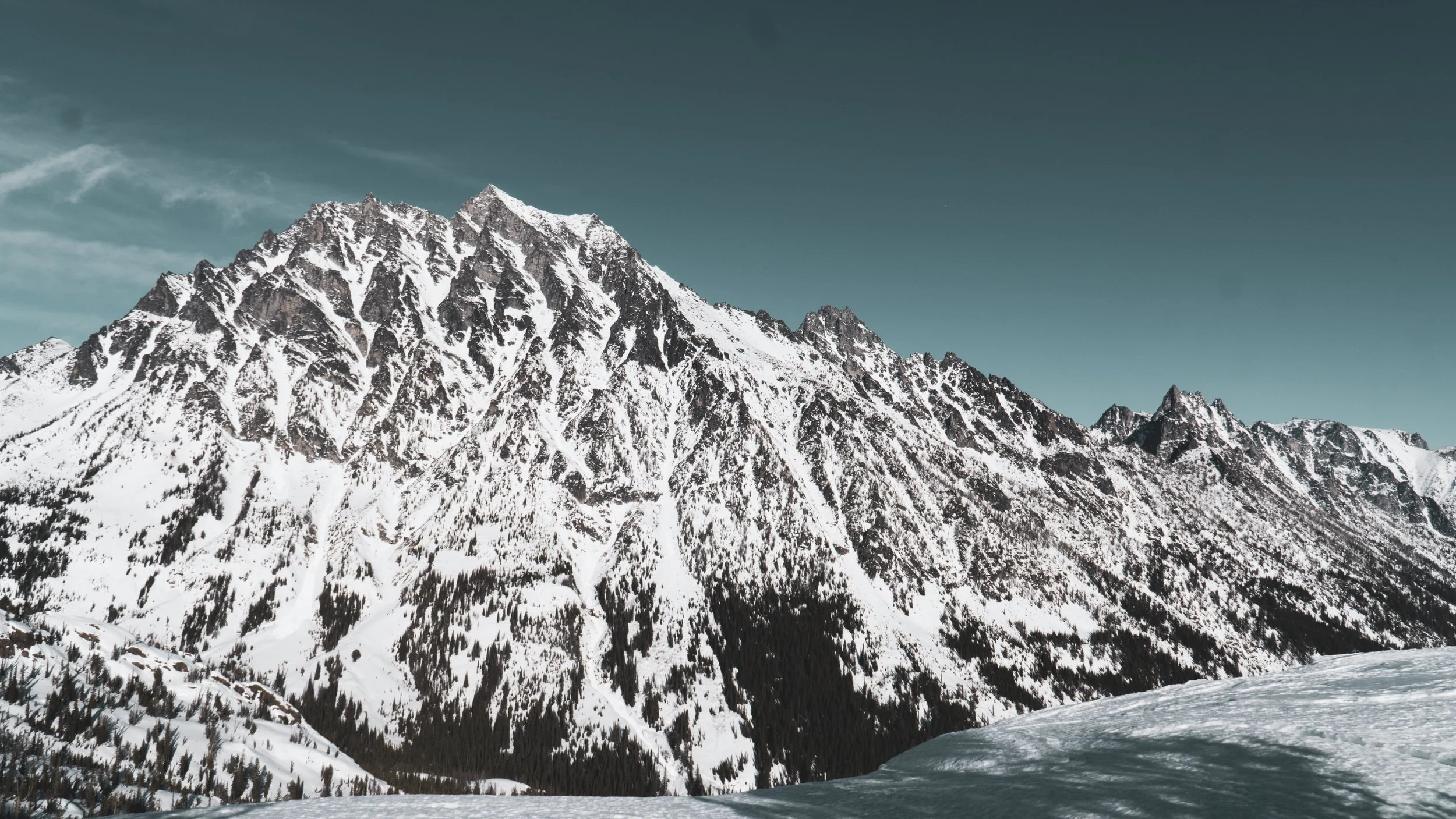 Snow-covered mountain range under a clear sky with some clouds.