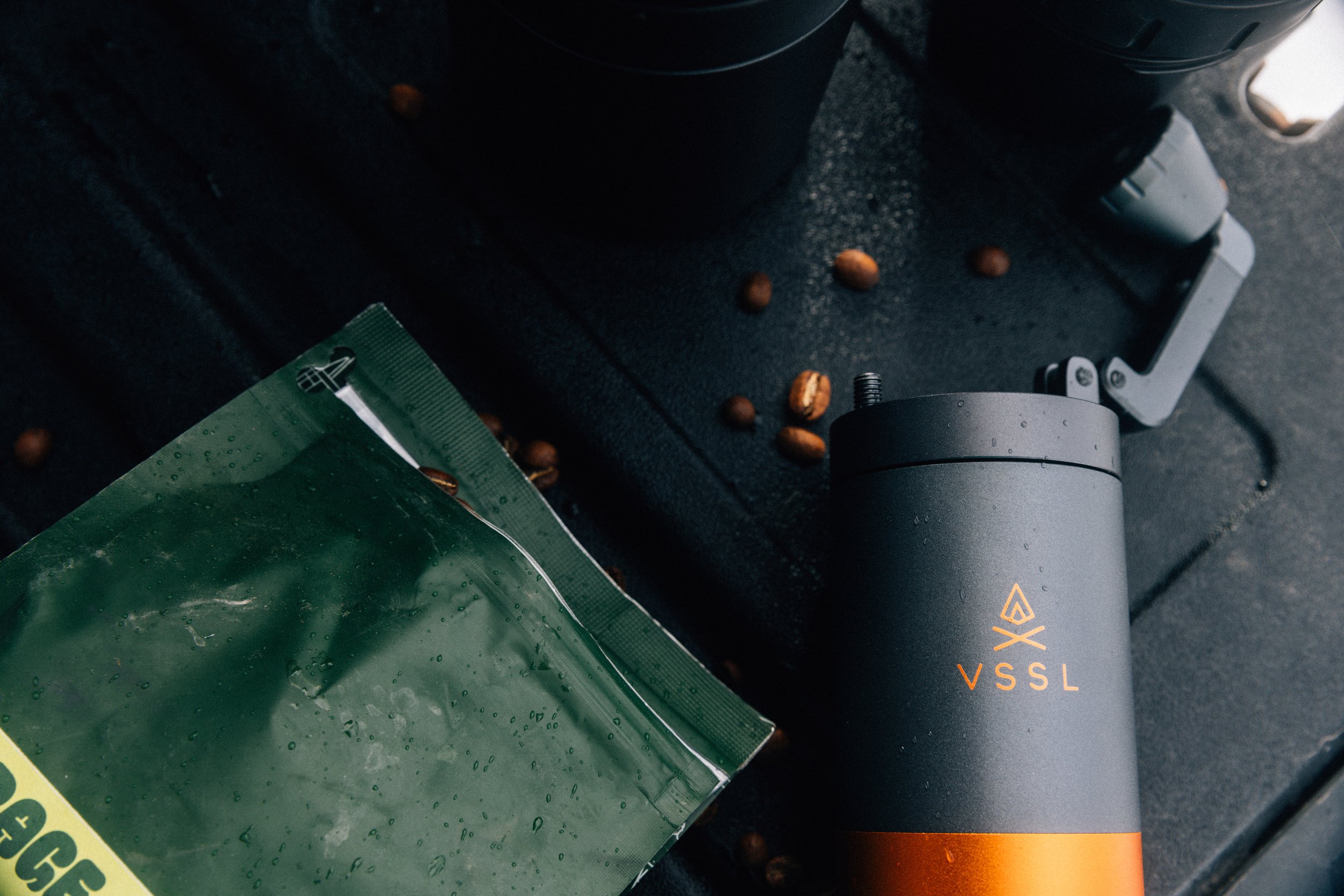 VSSL Java X2 coffee grinder resting beside a Motoring Coffee bag on a dark surface, orange accent ring catching the light.