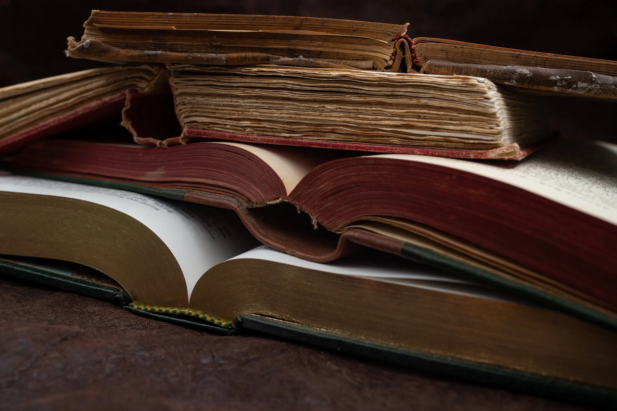 Close-up image of stacked old and new books with worn pages and covers on a dark surface.