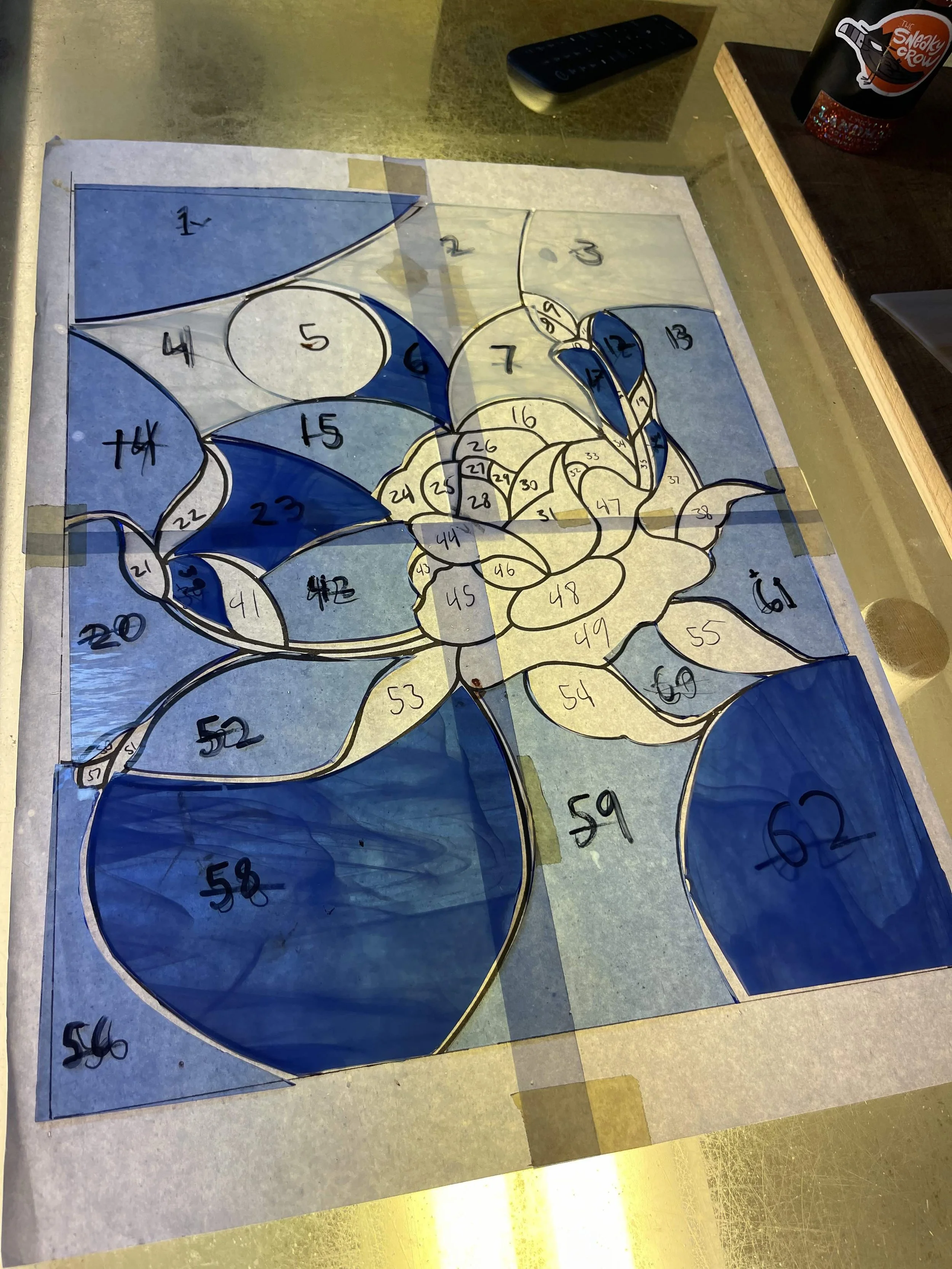 A mosaic puzzle of a flower with numbered pieces, blue and yellow sections, laid out on a table with tape around the edges.