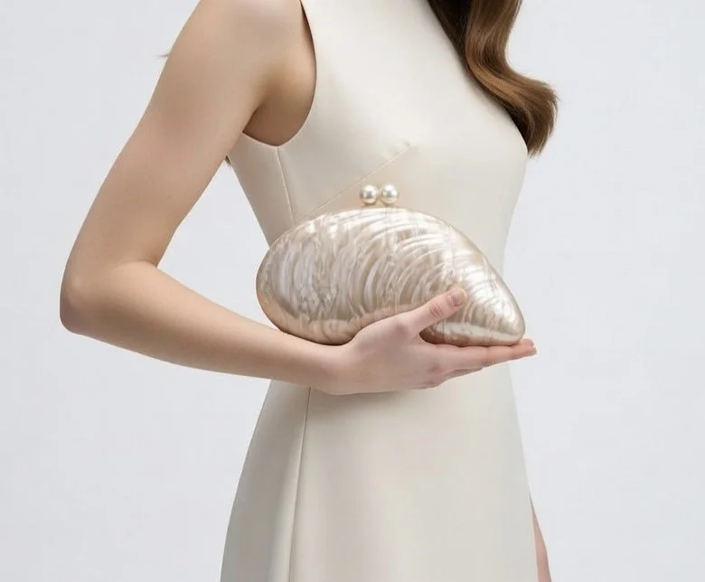A woman in a beige dress holding a large, seashell-shaped clutch purse with a pearl clasp.