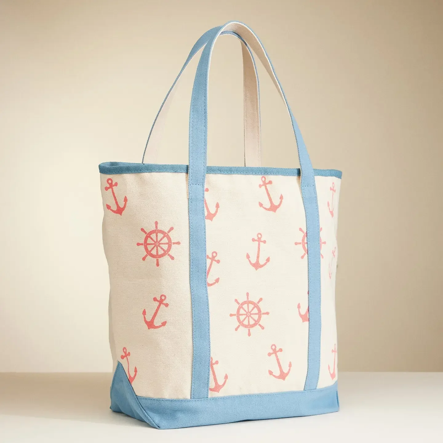 A tote bag with pink anchors and ship wheels pattern, featuring blue handles and trim, placed on a plain surface.
