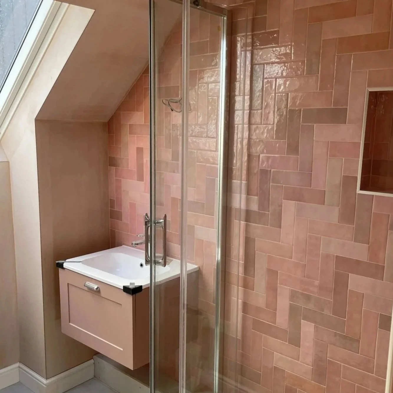 Bathroom with pink tiled wall, a small white sink, and a glass shower enclosure.