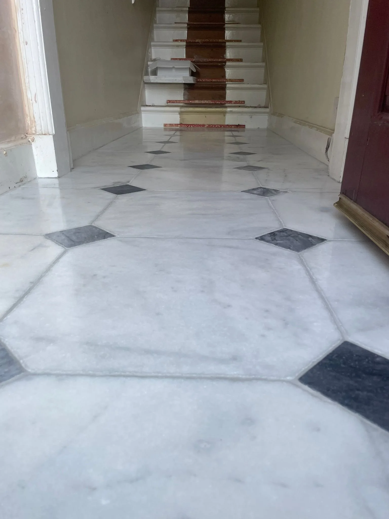 Marble and dark stone tiled flooring leading to a staircase with wooden steps, partially covered by red caution tape.